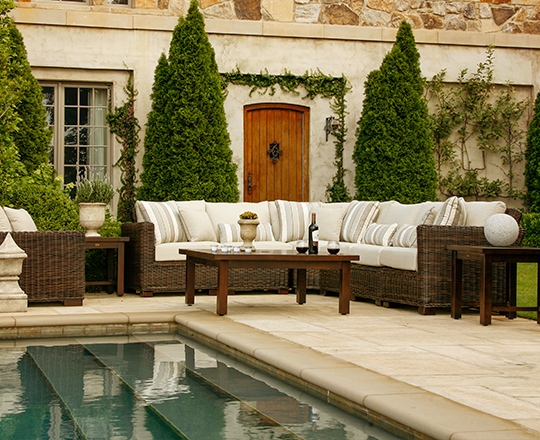 Brown wicker outdoor sofa in lush green backyard