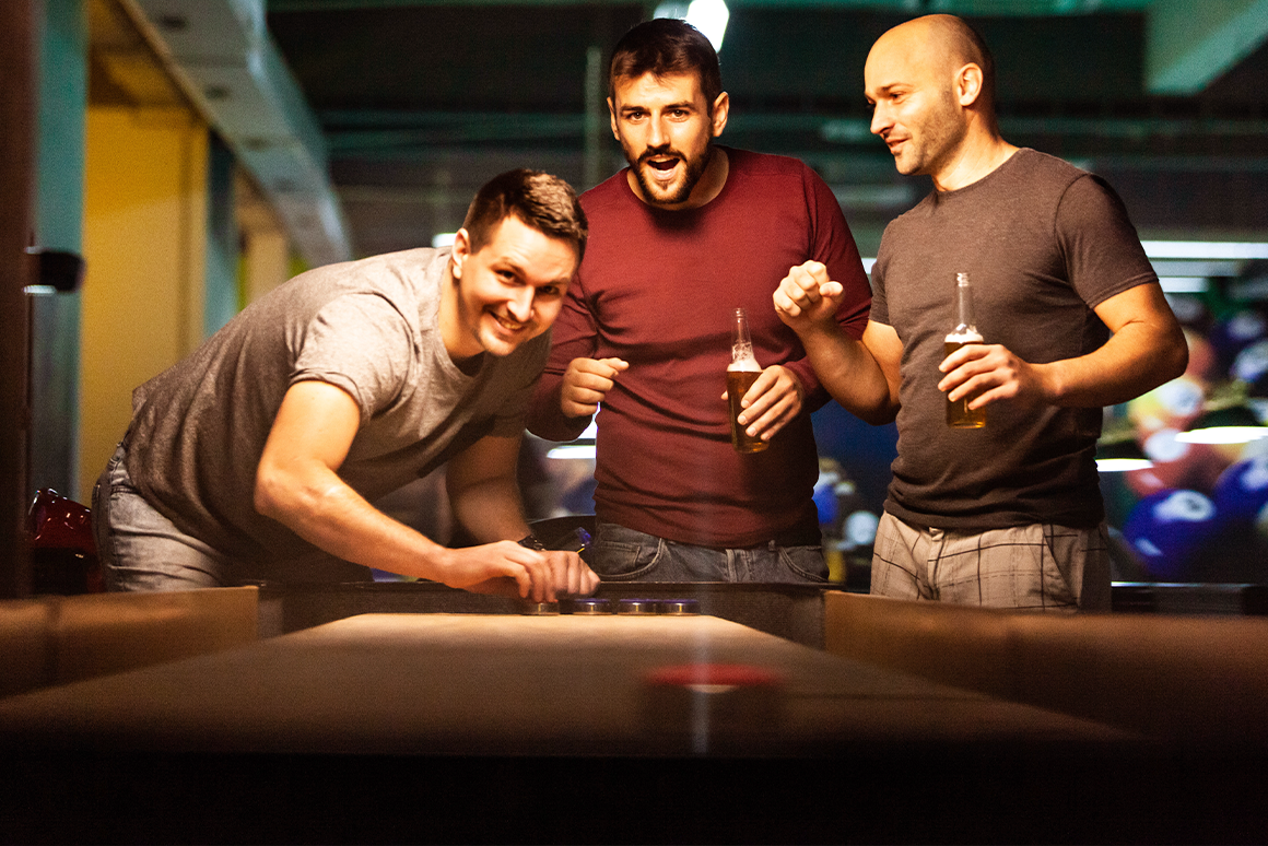 Guys drinking beer and playing shuffleboard in bar